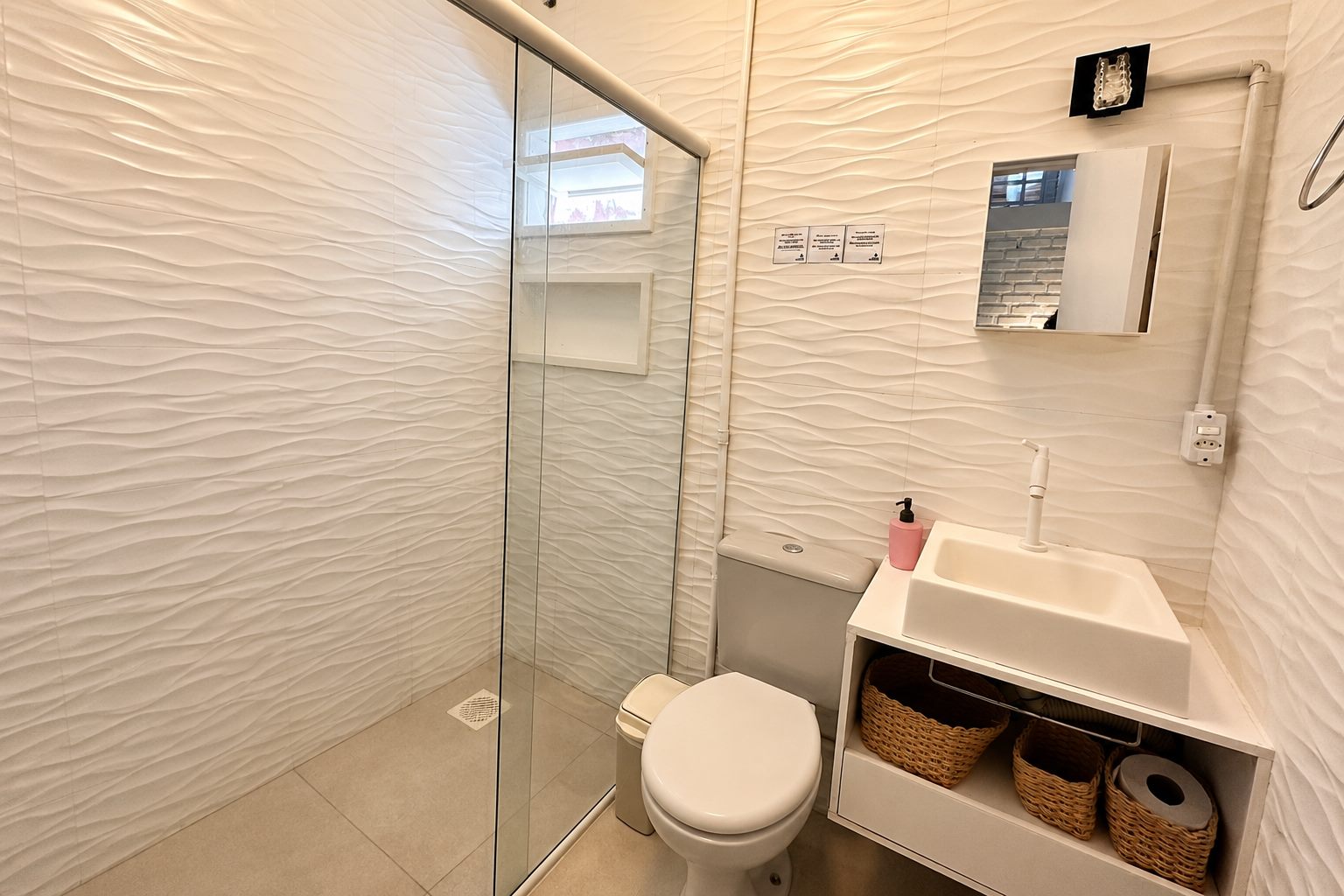 Banheiro privativo do apartamento, com box de vidro e revestimento texturizado branco