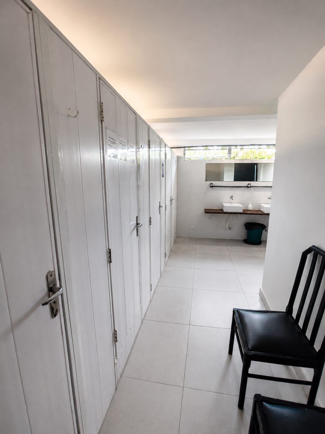 Corredor dos banheiros compartilhados, com boxes individuais e bancada de lavatórios ao fundo